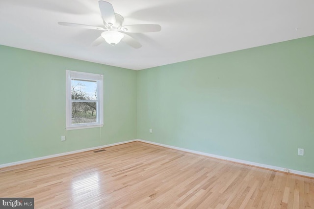 empty room featuring a ceiling fan, visible vents, baseboards, and wood finished floors