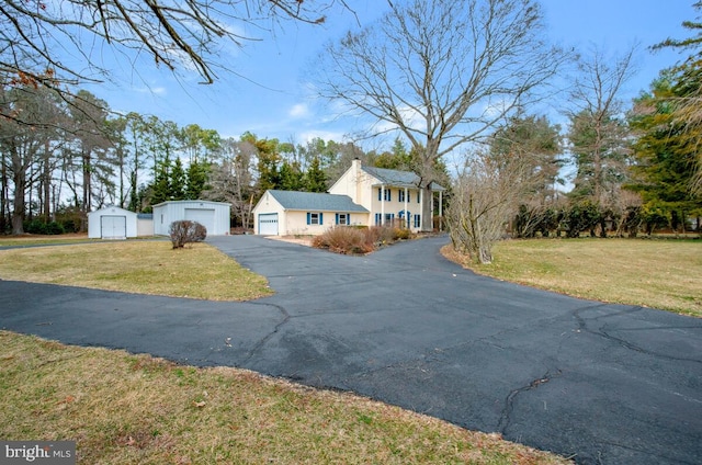 exterior space with an outbuilding, a front lawn, a chimney, and aphalt driveway