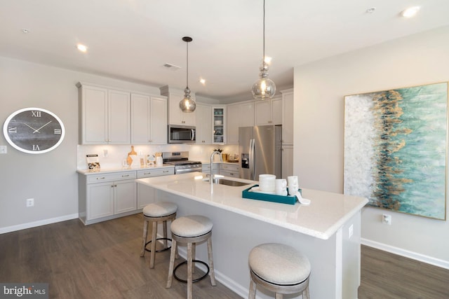 kitchen with a kitchen island with sink, stainless steel appliances, a sink, visible vents, and glass insert cabinets