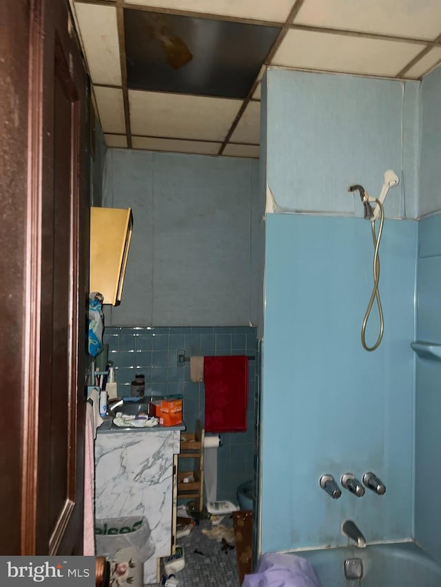 full bath with a drop ceiling, shower / tub combination, and tile walls