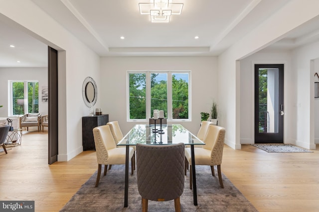 dining space with light wood-style floors, a raised ceiling, and baseboards