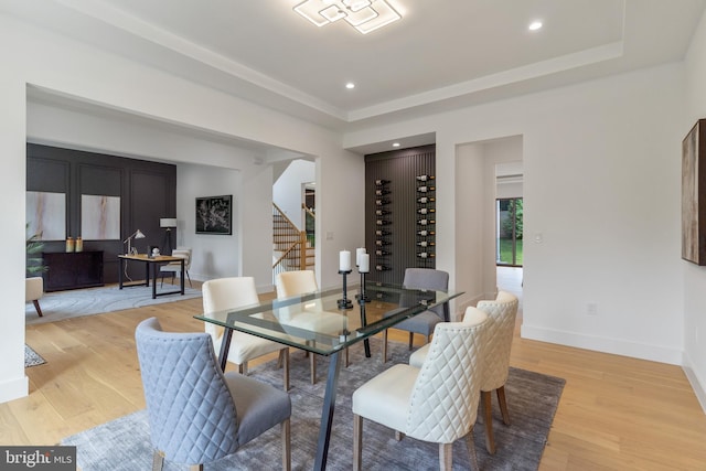 dining area featuring light wood-type flooring, a raised ceiling, baseboards, and stairs