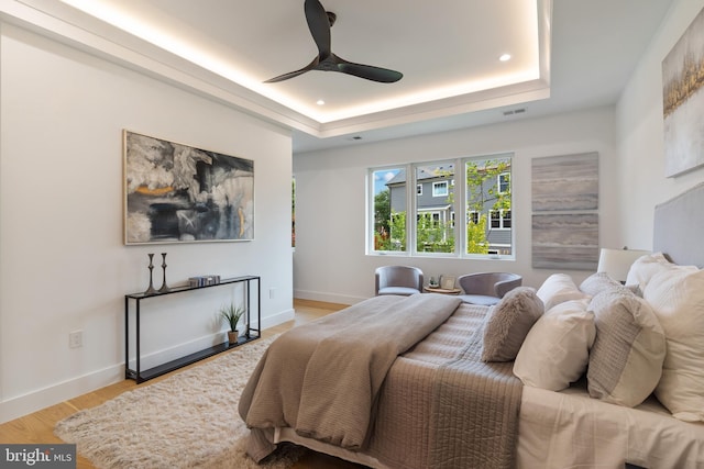 bedroom featuring light wood-style floors, ceiling fan, baseboards, and a raised ceiling