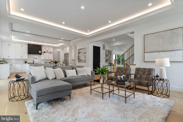 living room featuring recessed lighting, baseboards, stairway, light wood-type flooring, and a tray ceiling