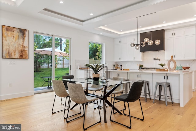 dining area featuring light wood-style flooring, a raised ceiling, and recessed lighting