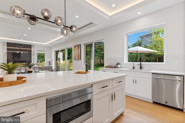 kitchen featuring stainless steel appliances, a sink, white cabinetry, a raised ceiling, and decorative light fixtures