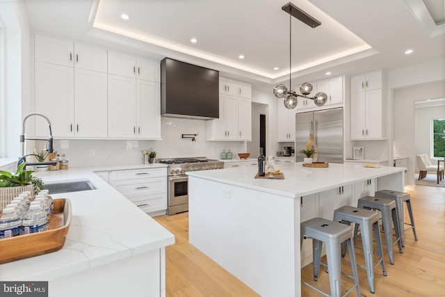 kitchen featuring premium appliances, white cabinets, a center island, wall chimney exhaust hood, and a raised ceiling