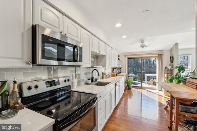 kitchen with backsplash, light wood-style flooring, appliances with stainless steel finishes, white cabinetry, and a sink