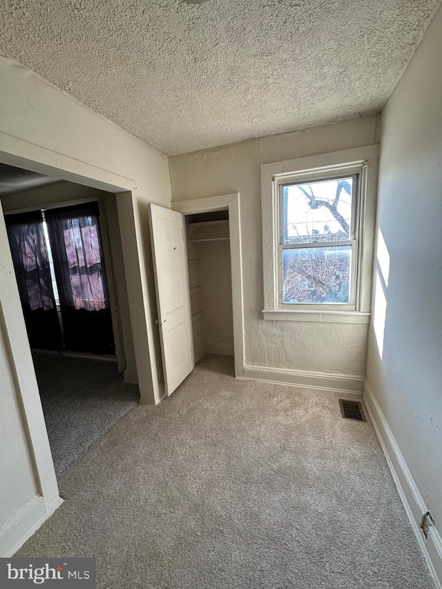 unfurnished bedroom featuring baseboards, visible vents, carpet, a textured ceiling, and a closet