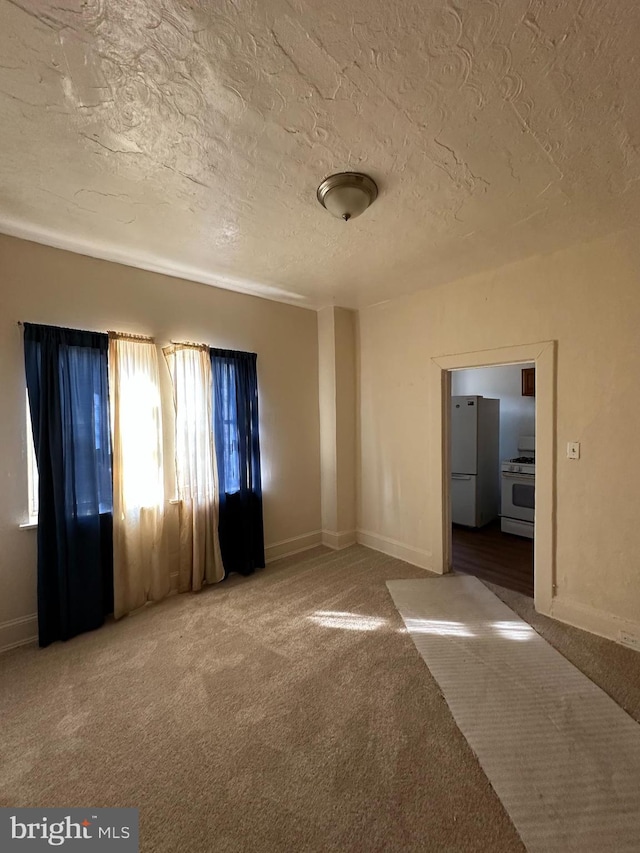 unfurnished room featuring carpet floors, a textured ceiling, and baseboards