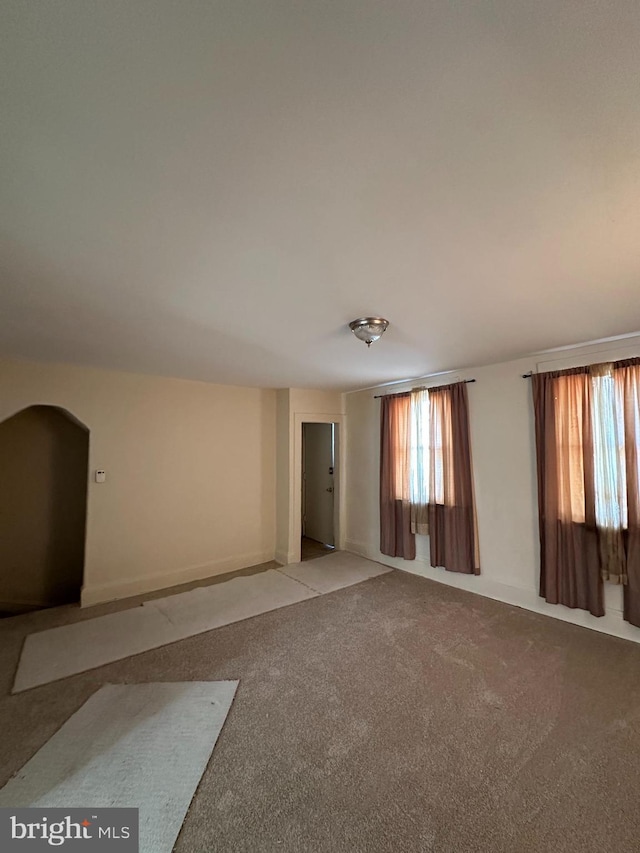 empty room with arched walkways and light colored carpet