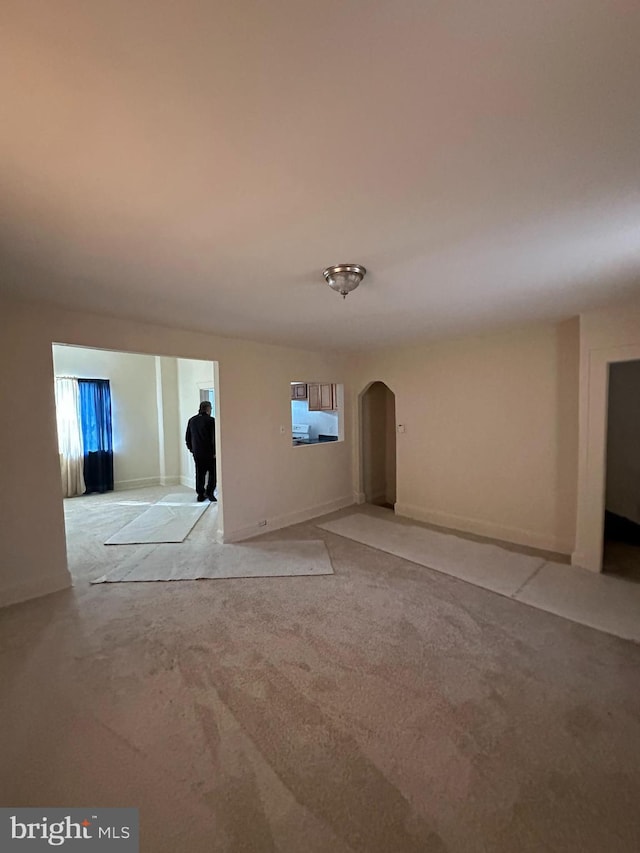 empty room featuring baseboards, arched walkways, a wealth of natural light, and light colored carpet