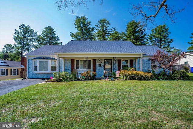 single story home with aphalt driveway, a porch, brick siding, roof with shingles, and a front yard