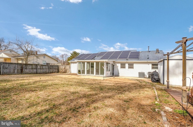 back of property with solar panels, a lawn, a sunroom, a fenced backyard, and an outdoor structure