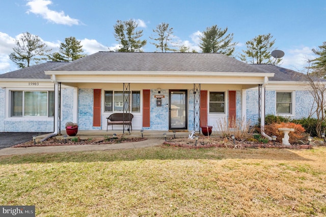 view of front facade with covered porch, brick siding, a front lawn, and roof with shingles