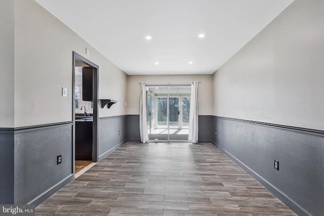 empty room with recessed lighting, a wainscoted wall, wood finished floors, a sink, and baseboards