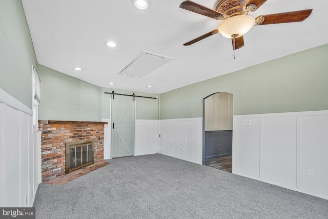 unfurnished living room featuring ceiling fan, a barn door, recessed lighting, a wainscoted wall, and carpet floors