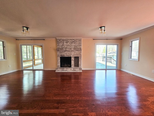 unfurnished living room with a brick fireplace, baseboards, ornamental molding, and wood finished floors