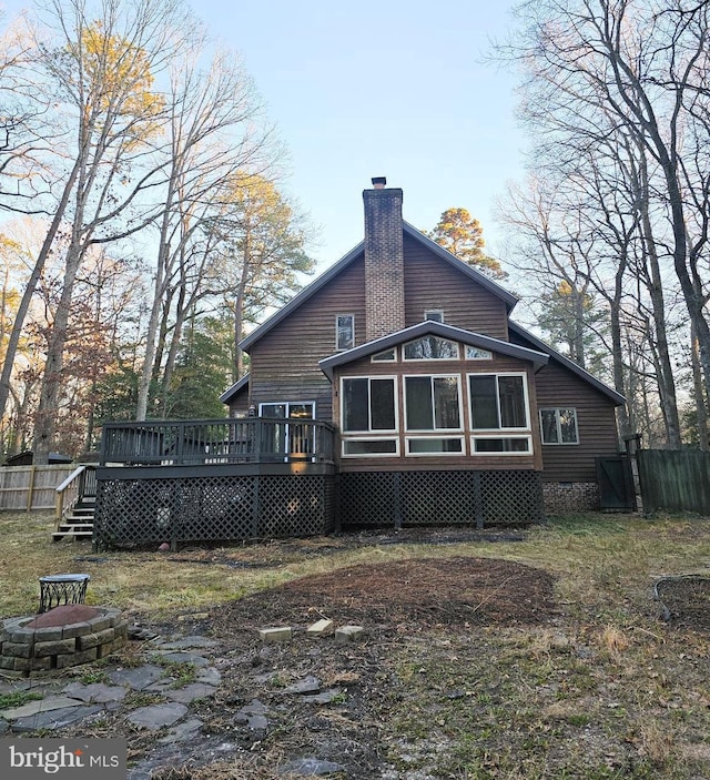 back of house with a chimney, a sunroom, fence, a fire pit, and a wooden deck