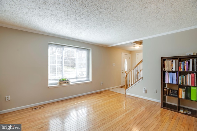 spare room featuring stairs, visible vents, a textured ceiling, baseboards, and hardwood / wood-style flooring