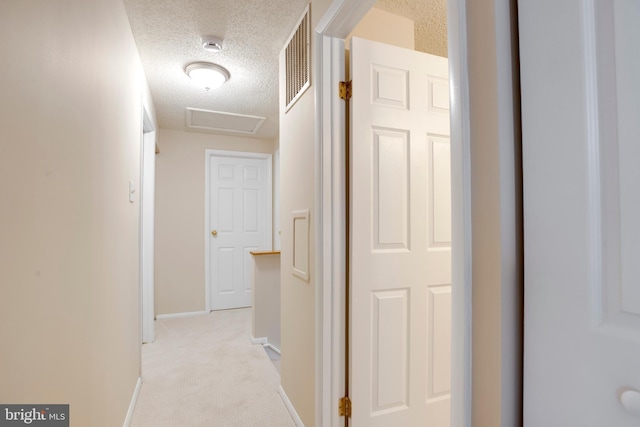 hall with light carpet, attic access, baseboards, visible vents, and a textured ceiling