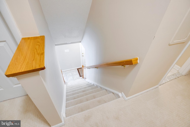 staircase with a textured ceiling, carpet flooring, and baseboards