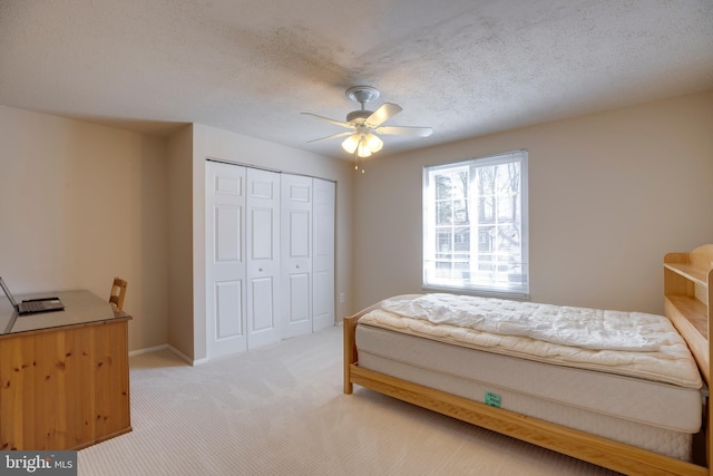 bedroom with ceiling fan, a textured ceiling, a closet, and light colored carpet