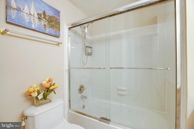 bathroom with a textured ceiling, toilet, and bath / shower combo with glass door