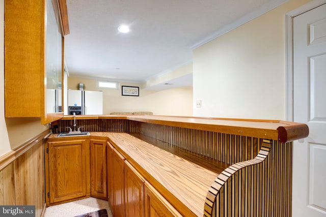 bar with white refrigerator with ice dispenser, ornamental molding, indoor wet bar, and a sink