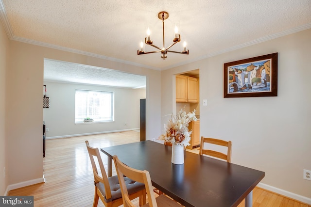 dining room with light wood-style floors, ornamental molding, a textured ceiling, and baseboards