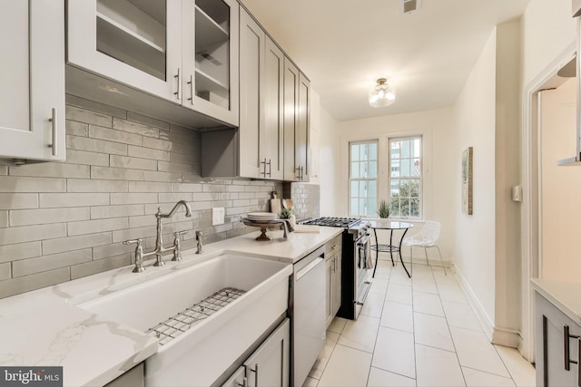 kitchen with light tile patterned floors, a sink, backsplash, dishwasher, and glass insert cabinets