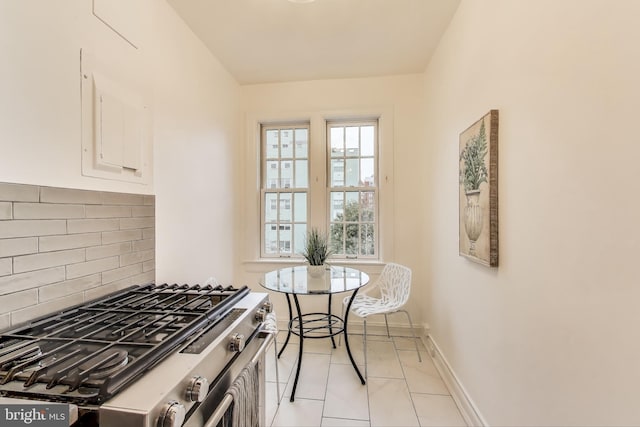 kitchen with light tile patterned floors, stainless steel gas range oven, baseboards, white cabinets, and decorative backsplash