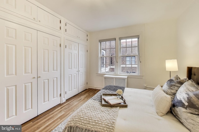 bedroom with light wood finished floors, radiator heating unit, and multiple closets