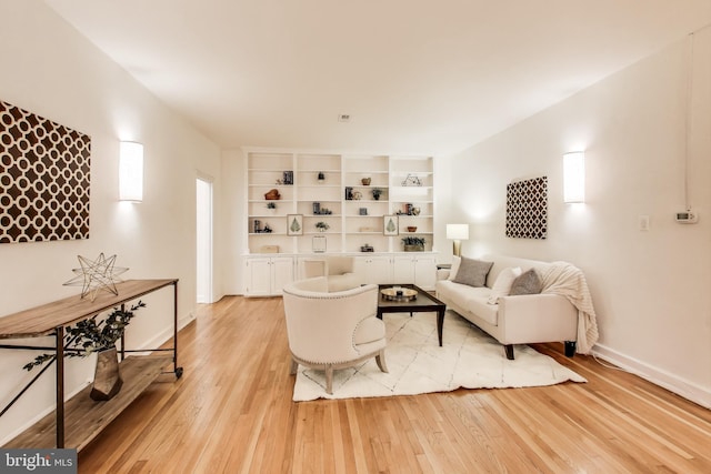 living room featuring baseboards, built in shelves, and light wood-style floors