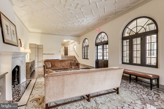 living area with a fireplace with raised hearth, ornamental molding, and arched walkways