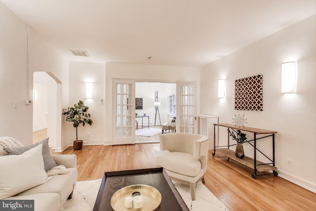 living area with arched walkways, wood finished floors, visible vents, baseboards, and french doors