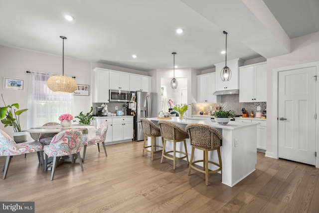 kitchen with stainless steel appliances, light countertops, a kitchen island with sink, and white cabinetry