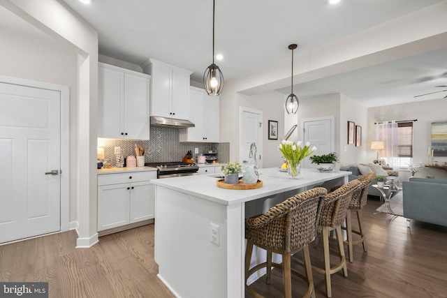 kitchen featuring under cabinet range hood, white cabinetry, open floor plan, light countertops, and a center island with sink