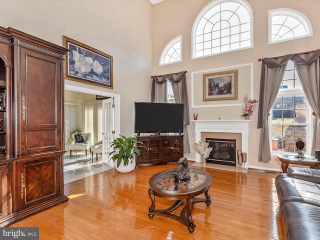 living room with a fireplace with flush hearth, light wood-style flooring, and a towering ceiling