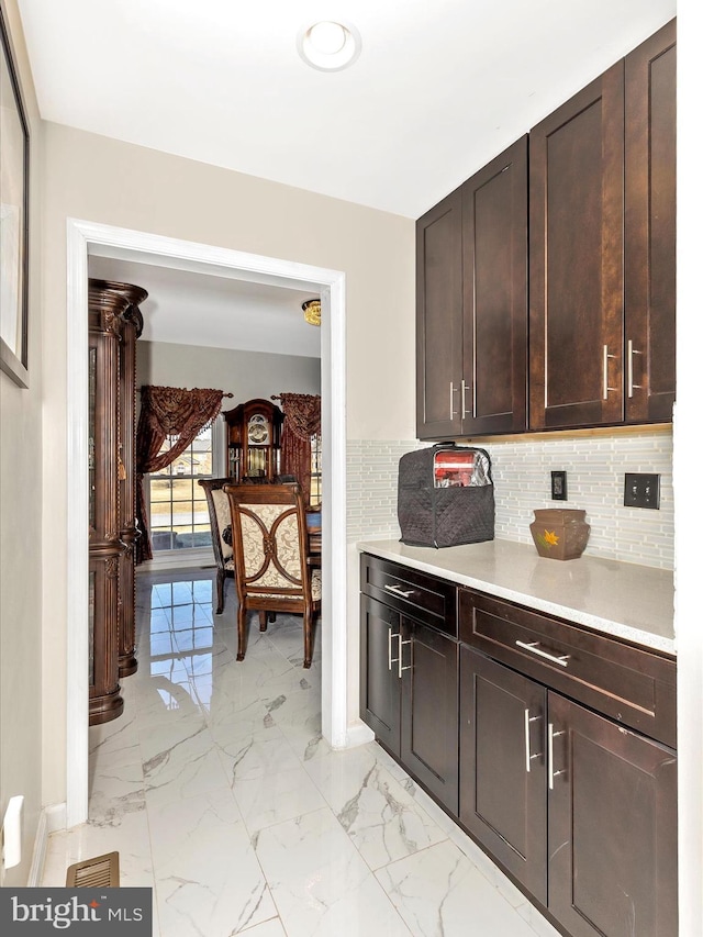 kitchen with marble finish floor, tasteful backsplash, light countertops, baseboards, and dark brown cabinets