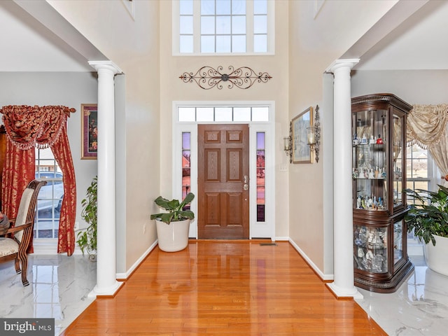 foyer entrance with light wood-type flooring, baseboards, a towering ceiling, and ornate columns