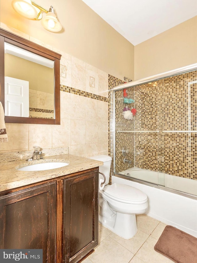 full bathroom featuring vanity, shower / bath combination with glass door, tile patterned flooring, tile walls, and toilet