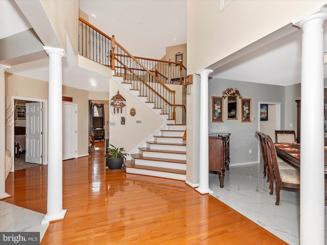 entrance foyer featuring stairway, light wood-type flooring, ornate columns, and a towering ceiling