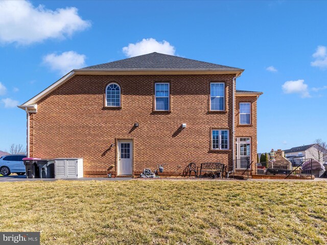 back of house with brick siding, a lawn, and a shingled roof