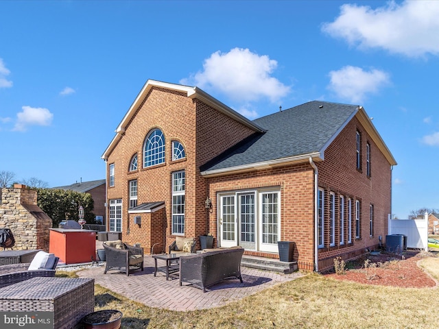 back of property with brick siding, roof with shingles, a lawn, an outdoor hangout area, and a patio area