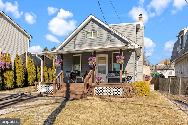 bungalow featuring covered porch, a front lawn, a chimney, and fence