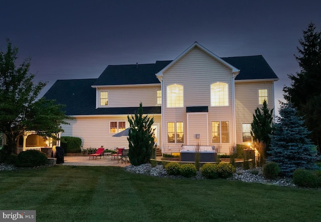 back of house at twilight with a patio area, a hot tub, and a yard