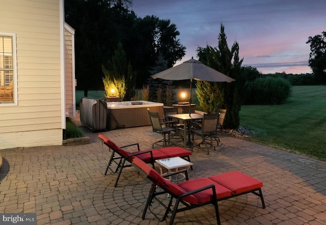 patio terrace at dusk featuring outdoor dining area, a lawn, and a hot tub