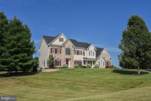 view of front facade with central air condition unit, stone siding, and a front yard