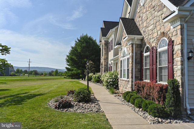 view of side of home with a lawn, stone siding, and roof with shingles